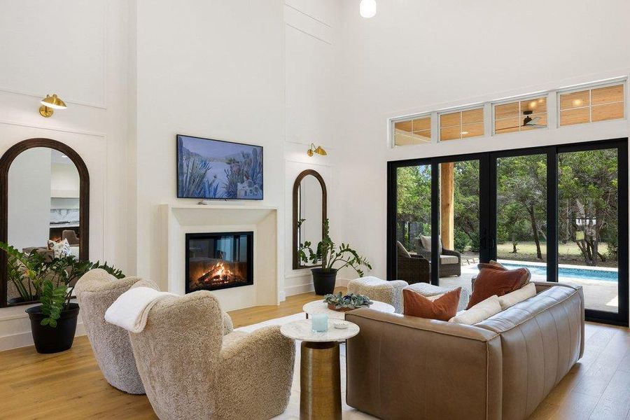 A spacious living room features soaring ceilings and an elegant fireplace, complemented by a serene view of the outdoor pool. A spacious living room features soaring ceilings and an elegant fireplace, complemented by a serene view of the outdoor pool.