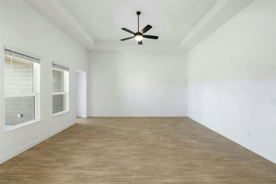 Spacious room featuring wood-finish tile flooring, a tray ceiling, an overhead fan with integrated lighting, and multiple windows