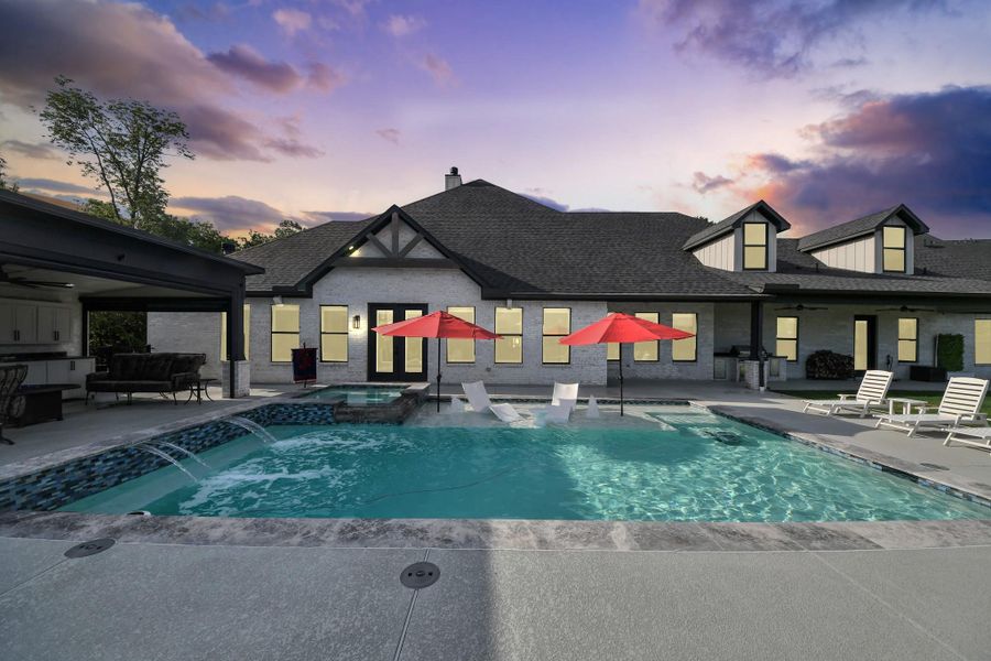 Experience luxury outdoor living with a stunning backyard oasis featuring a sparkling pool, dual spa waterfalls, and elegant lounge areas, all set against a beautiful sunset sky.
