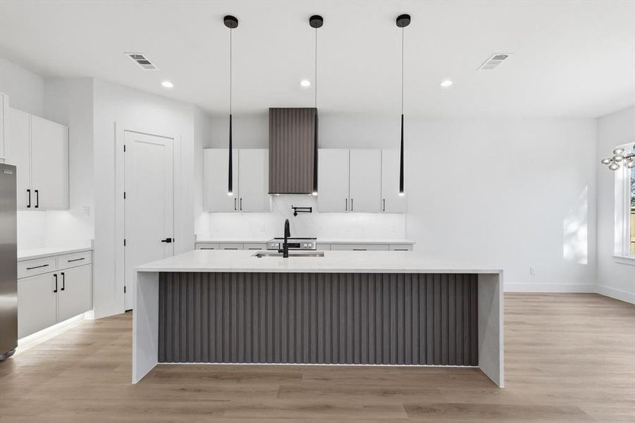 Kitchen with white cabinetry, light stone counters, a large island, hanging light fixtures, and recessed lighting Kitchen with white cabinetry, light stone counters, a large island, hanging light fixtures, and recessed lighting