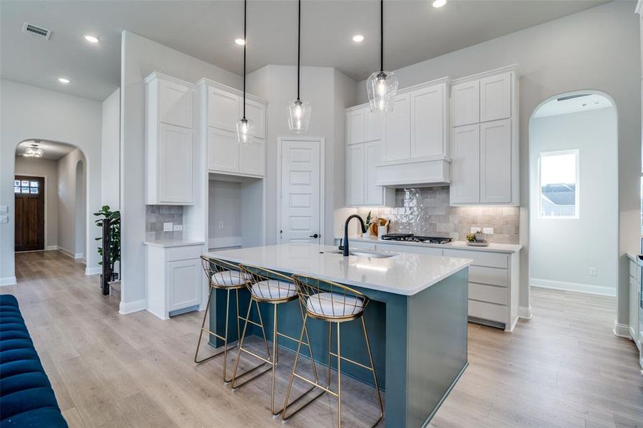 Kitchen featuring a center island with sink, decorative backsplash, white cabinetry, and sink