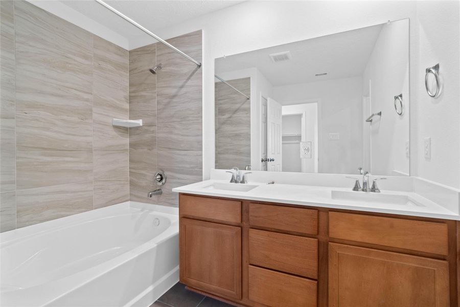 This bathroom blends charm and functionality with elegant design details. The oversized tub/shower combo with tile surround, dual sinks, stained cabinetry, mirror and sleek fixtures makes this space both practical and gorgeous. This bathroom blends charm and functionality with elegant design details. The oversized tub/shower combo with tile surround, dual sinks, stained cabinetry, mirror and sleek fixtures makes this space both practical and gorgeous.