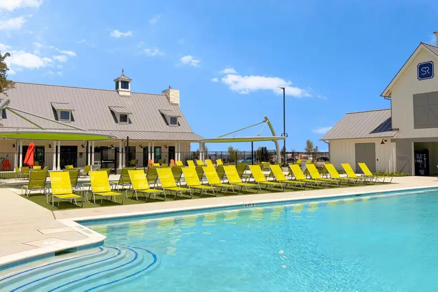 A sparkling community swimming pool sits adjacent to modern clubhouse facilities under a clear sky.