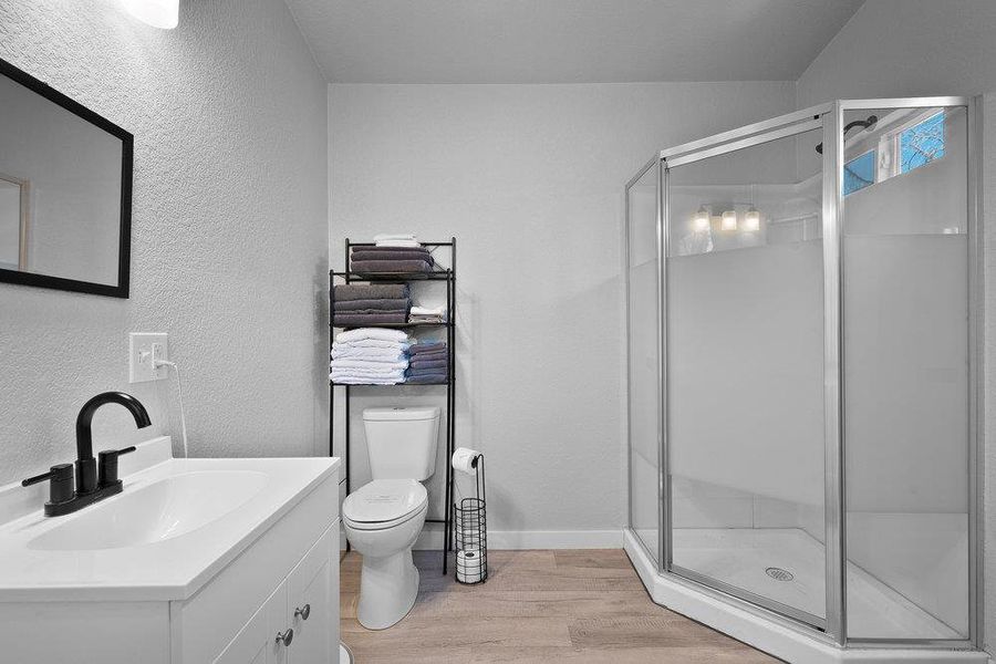 Full bath featuring light wood finished floors, vanity, a shower stall, and a textured wall.