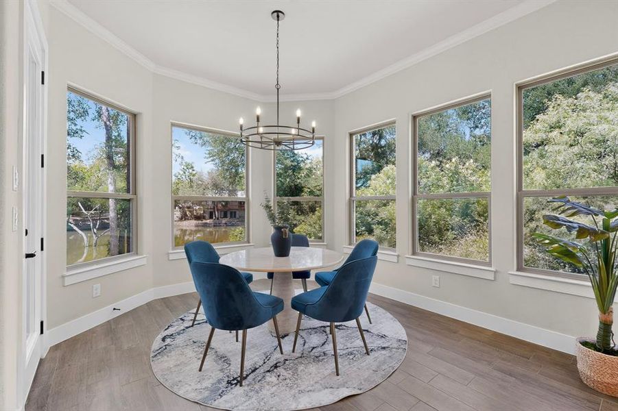 Dining area with wood-finish flooring, ample natural light from multiple windows, and a contemporary chandelier