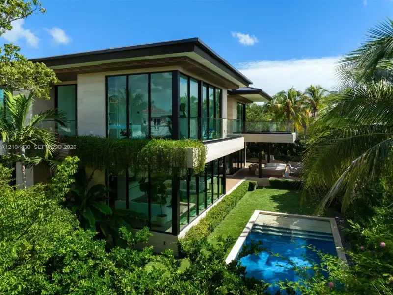 Modern architectural residence featuring floor-to-ceiling windows, stone exterior cladding, a second-story glass-railed balcony, an in-ground swimming pool, and manicured landscaping