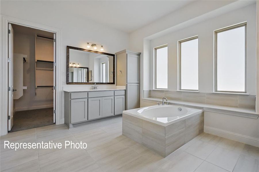 Bathroom featuring a relaxing tiled tub, vanity, and tile patterned flooring