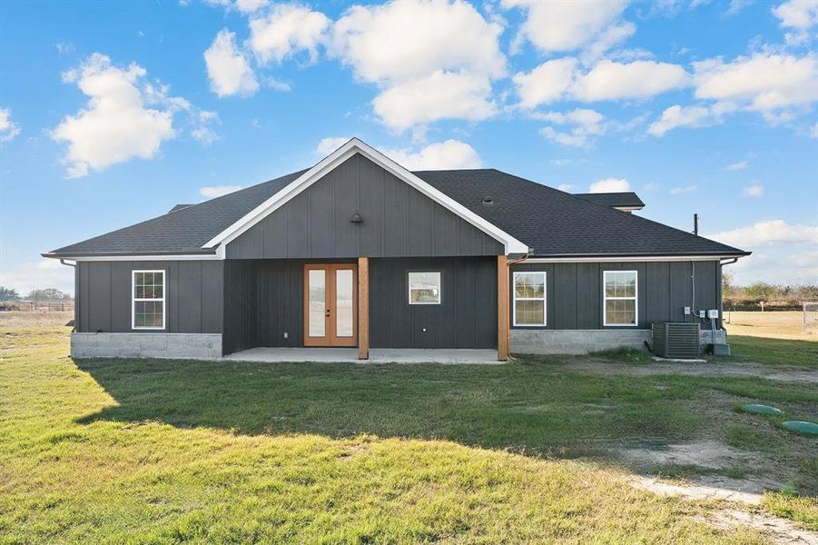 Back of house with a shingled roof, a patio, a lawn, and french doors