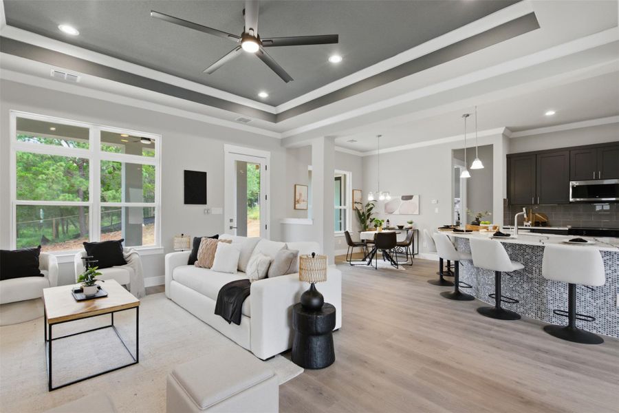 An inviting open-concept living area boasts a modern ceiling fan, large windows, and seamless transitions to dining and kitchen spaces. An inviting open-concept living area boasts a modern ceiling fan, large windows, and seamless transitions to dining and kitchen spaces.