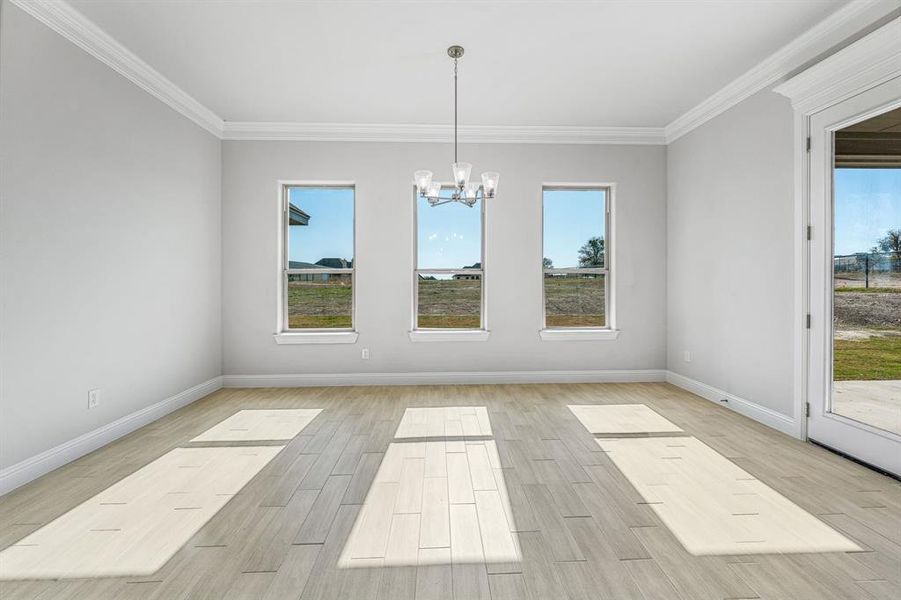 Unfurnished dining area featuring wood finish floors, healthy amount of natural light, crown molding, and a chandelier