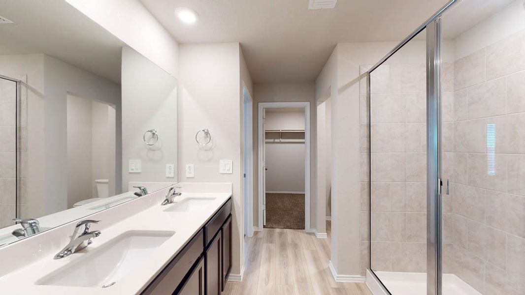 A well-lit primary bathroom features a dual vanity, a large walk-in shower, and light hardwood-style flooring. A well-lit primary bathroom features a dual vanity, a large walk-in shower, and light hardwood-style flooring.