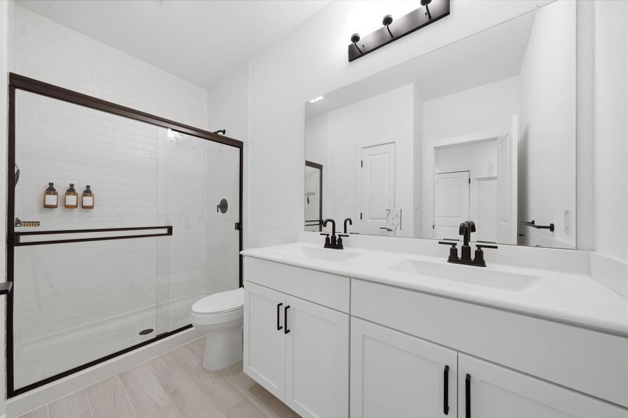 The second bathroom features a modern design with a spacious double vanity, sleek black fixtures, and a large mirror. located just off the foyer by the guest room. Includes a glass-enclosed shower with stylish tile work and ample natural light, creating a clean and contemporary feel.