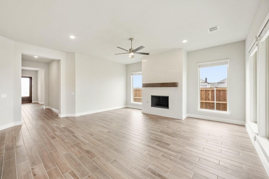 Open living room with wood-look tile floors, ceiling fan, and white fireplace with wood mantel