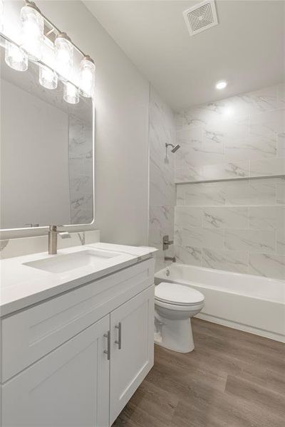 Full bathroom with toilet, tiled shower / bath, hardwood / wood-style flooring, and vanity