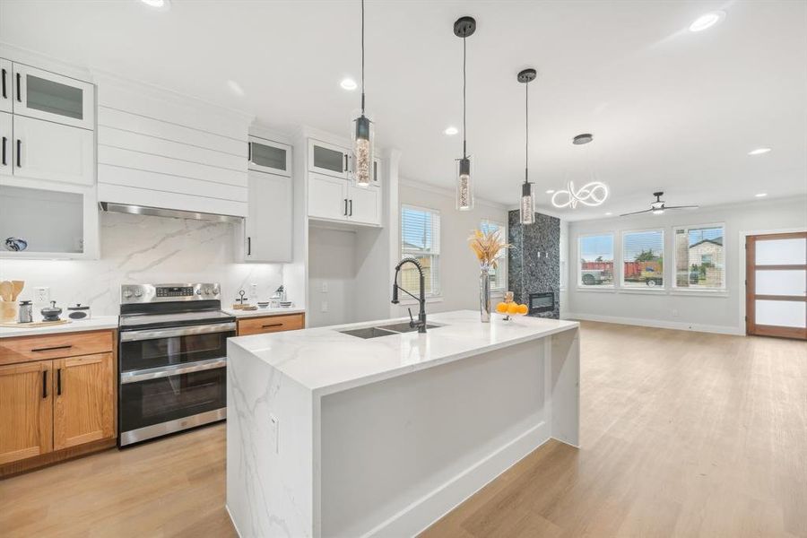 Kitchen with a fireplace, white cabinetry, stainless steel electric stove, light stone counters, and sink