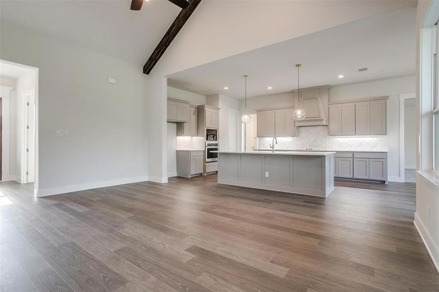 Kitchen featuring hardwood / wood-style floors, stainless steel oven, gray cabinetry, ceiling fan, and a center island with sink