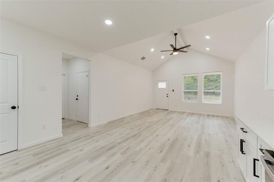 Unfurnished living room featuring light wood-type flooring, ceiling fan, and lofted ceiling with beams