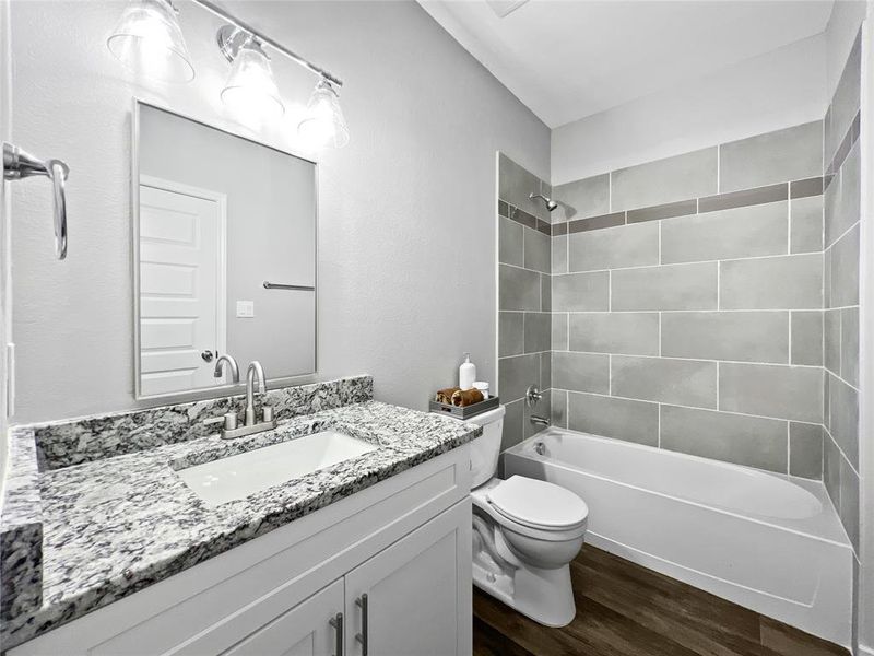 Full bathroom with hardwood / wood-style floors, vanity, tiled shower / bath combo, and toilet