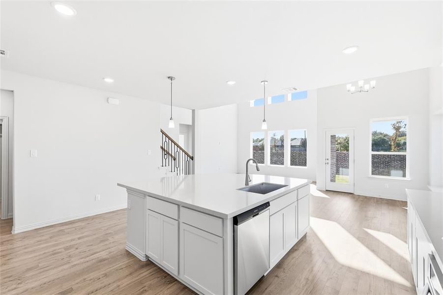 Kitchen with white cabinetry, decorative light fixtures, dishwasher, light wood finished floors, and a kitchen island with sink