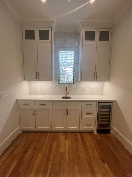 Kitchen with beverage cooler, crown molding, hardwood / wood-style floors, sink, and tasteful backsplash