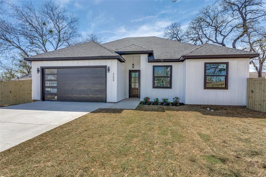 View of front of home featuring a shingled roof, fence, concrete driveway, a front yard, and a garage