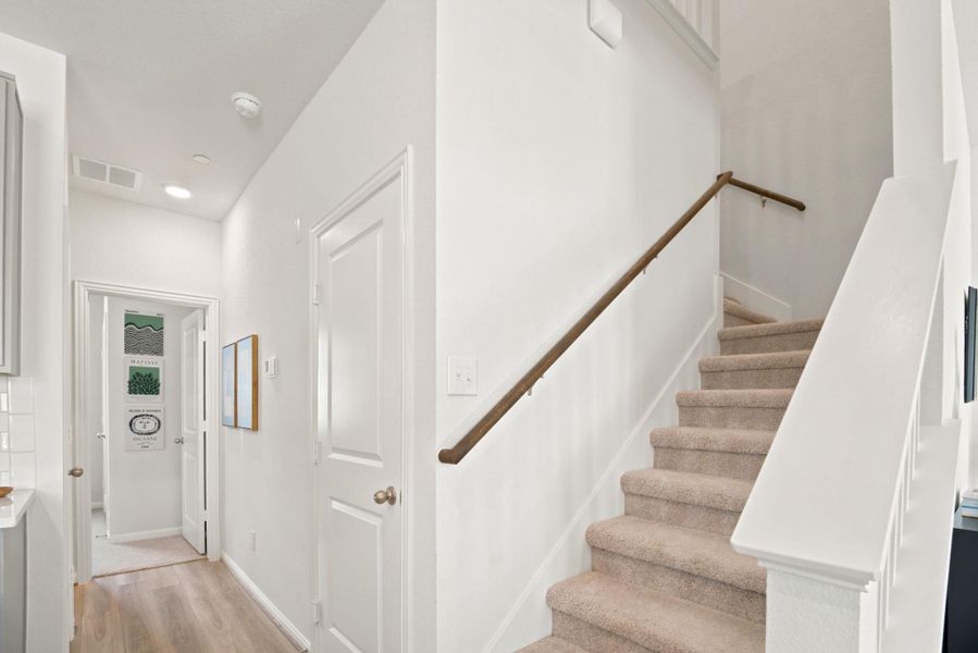 Plush carpeted stairs ascend from a hallway detailed with wood-toned flooring and high ceilings.