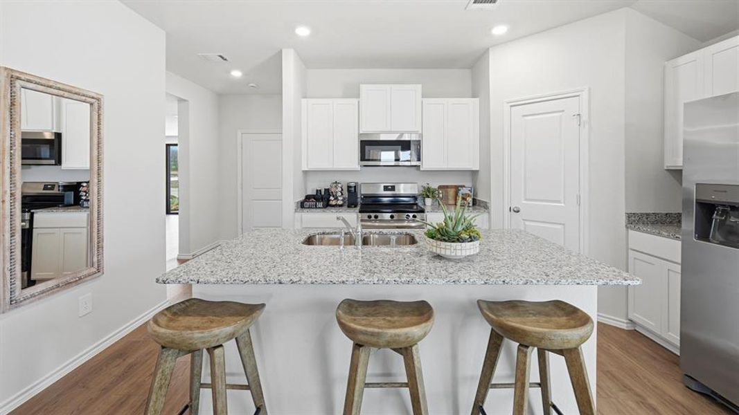 The kitchen features an island with a sink and a granite countertop, white cabinetry, and stainless steel appliances including a range and refrigerator