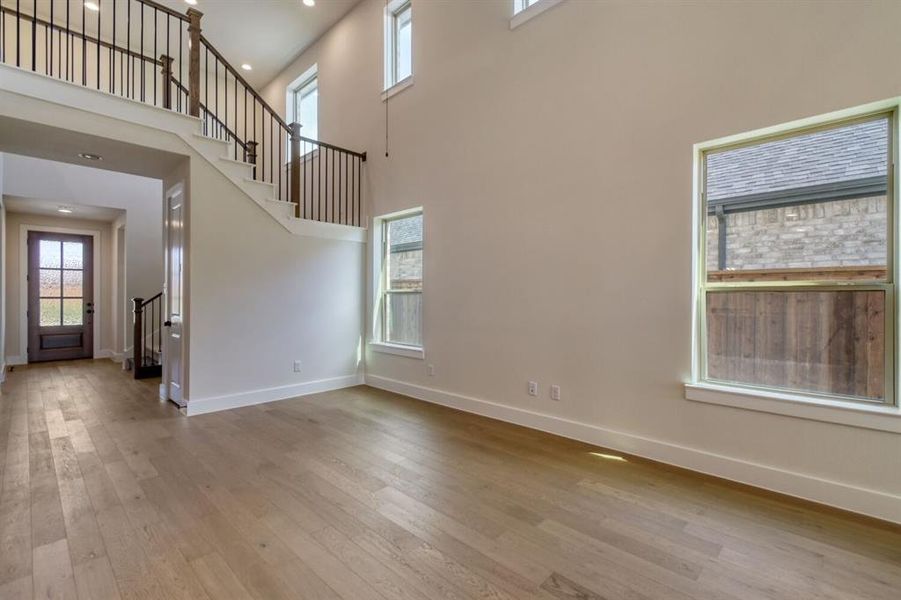 Unfurnished living room with light wood finished floors, a high ceiling, and recessed lighting Unfurnished living room with light wood finished floors, a high ceiling, and recessed lighting