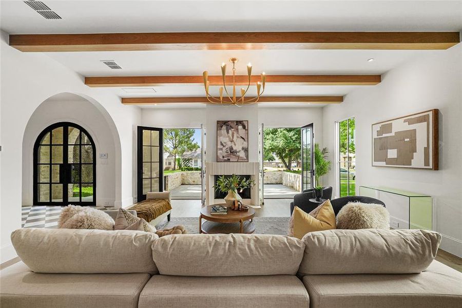 Great room featuring exposed wood ceiling beams, a central chandelier, and a fireplace with a textured surround