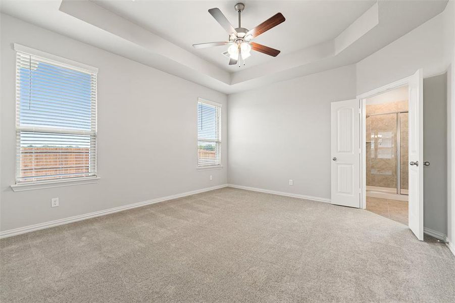 Spare room featuring a tray ceiling, light colored carpet, and a ceiling fan Spare room featuring a tray ceiling, light colored carpet, and a ceiling fan