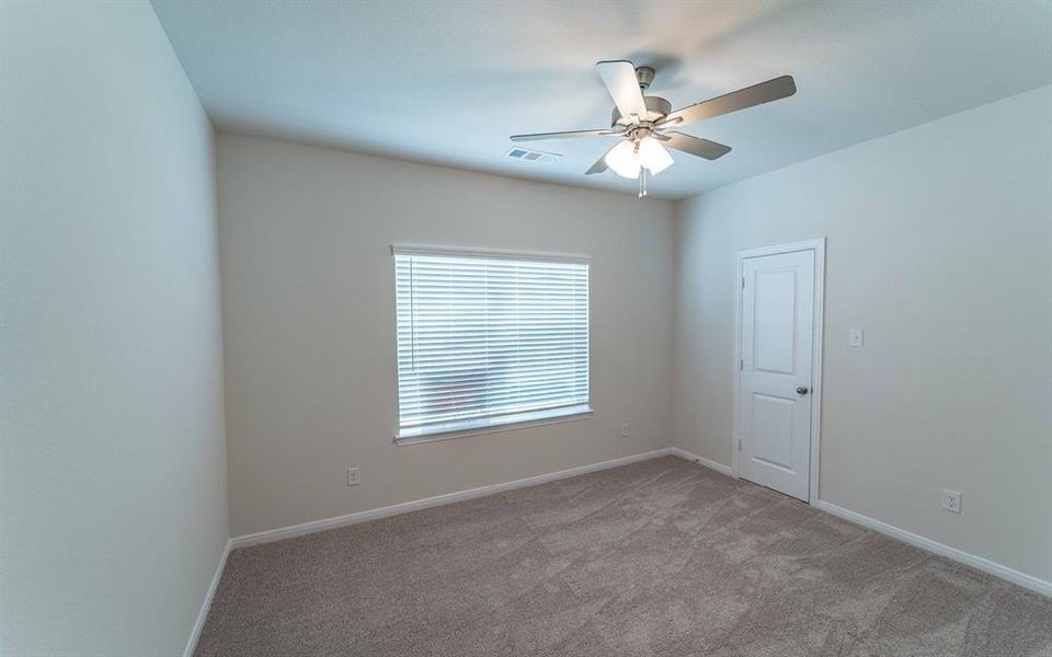 Carpeted room featuring neutral-toned walls, a window with blinds, a white paneled door, and a ceiling fan with integrated lighting