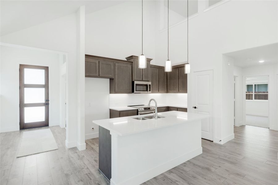 Open kitchen with white island, dark brown cabinets, pendant lights, and high ceilings Open kitchen with white island, dark brown cabinets, pendant lights, and high ceilings