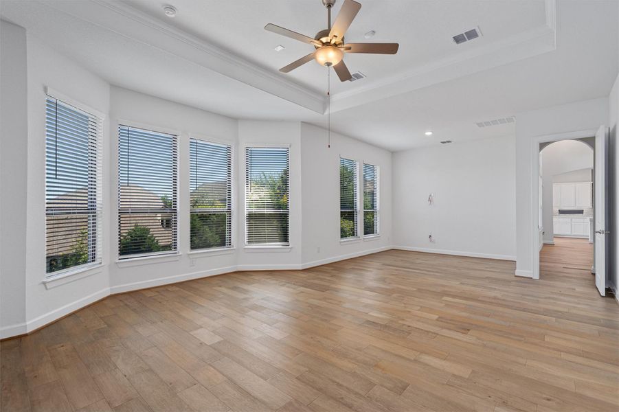 Spacious room featuring light wood-finish flooring, a tray ceiling with a built-in ceiling fan, recessed lighting, and a bay window configuration with multiple windows