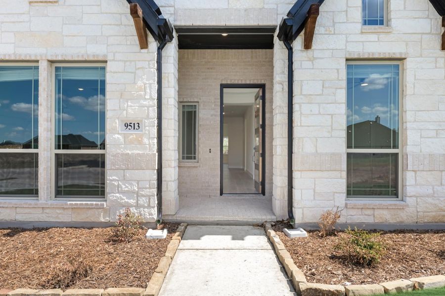 Home entrance with light stone exterior, open front door, black trim, and concrete walkway at address 9513