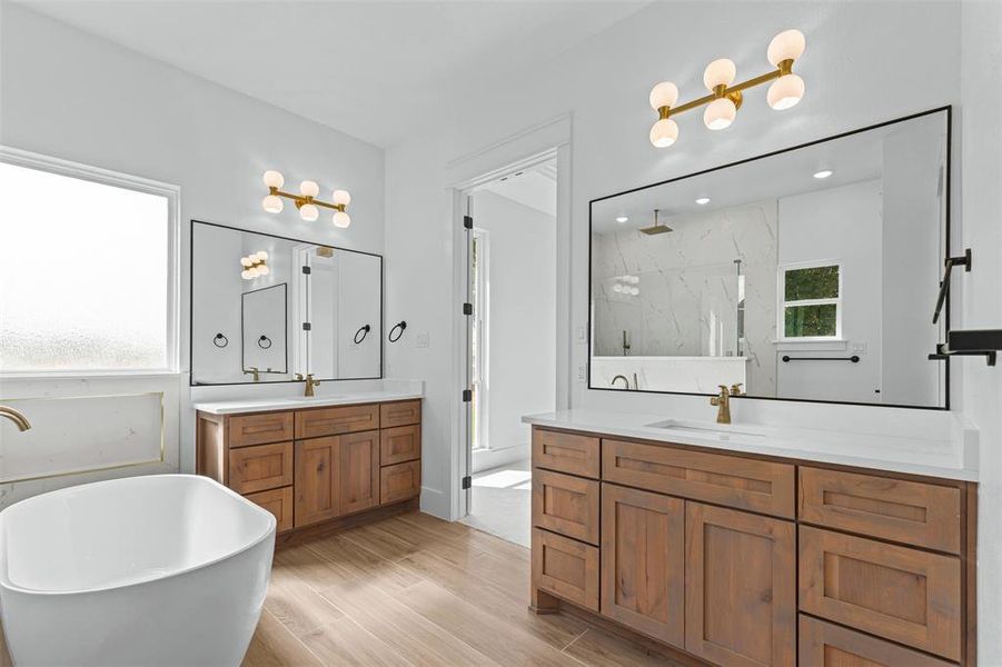 Full bathroom featuring a marble finish shower, two vanities, a soaking tub, and light wood-style flooring