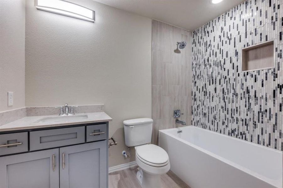 Full bathroom with hardwood / wood-style flooring, tiled shower / bath, vanity, and toilet