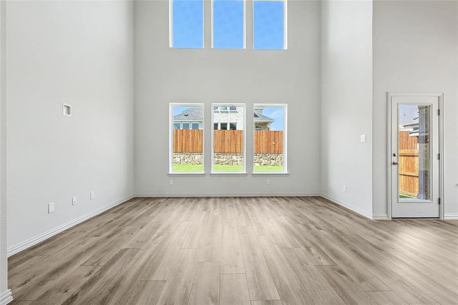 Unfurnished living room with light wood-style flooring, a towering ceiling, and plenty of natural light Unfurnished living room with light wood-style flooring, a towering ceiling, and plenty of natural light