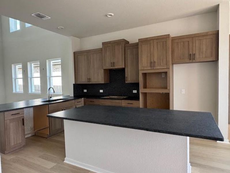 Kitchen with a center island, backsplash, brown cabinetry, light wood finished floors, and a kitchen bar Kitchen with a center island, backsplash, brown cabinetry, light wood finished floors, and a kitchen bar