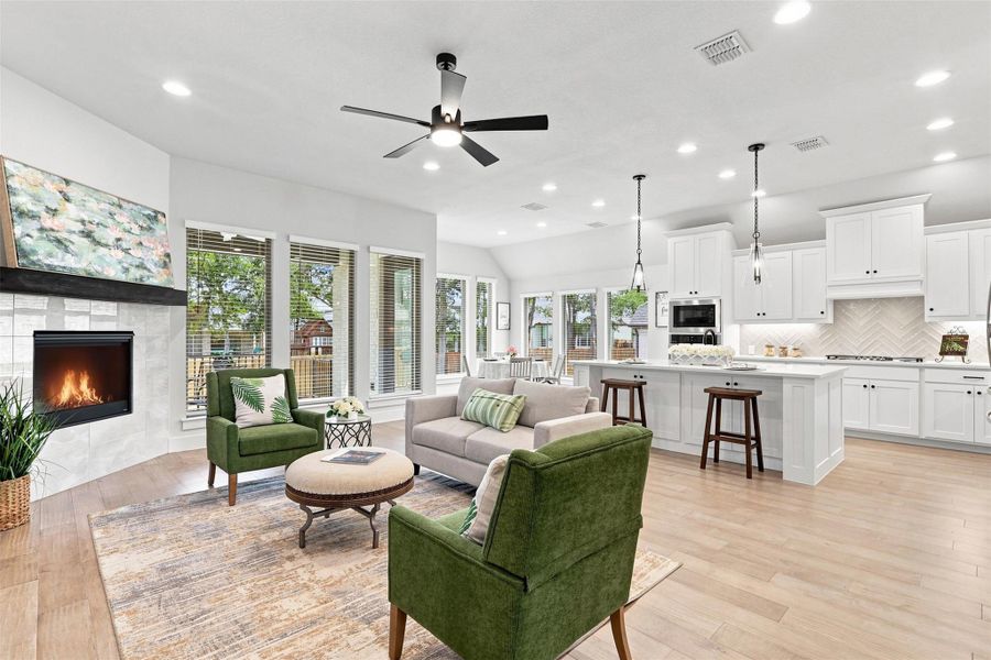 An open-concept living space presents a modern fireplace, light faux-wood tile flooring, and abundant natural light from numerous windows.