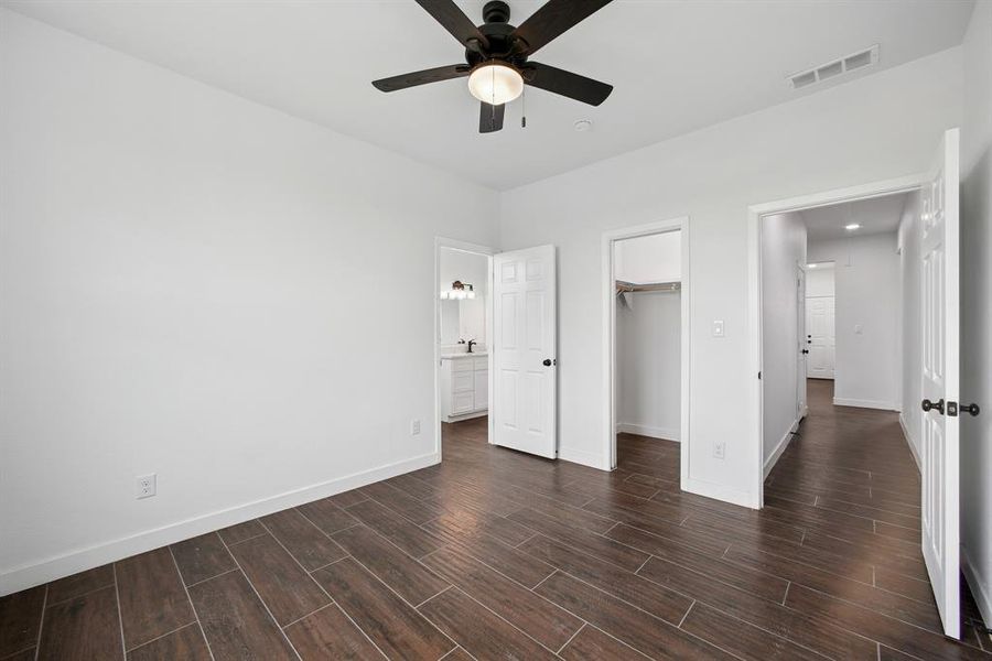 Unfurnished bedroom with wood finish floors, a spacious closet, ceiling fan, and ensuite bathroom