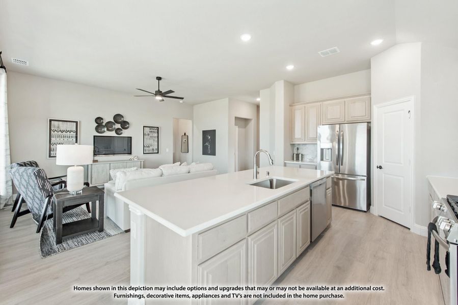 Open-concept kitchen with large island, white cabinets, stainless steel appliances, and adjoining living room with ceiling fan. Open-concept kitchen with large island, white cabinets, stainless steel appliances, and adjoining living room with ceiling fan.