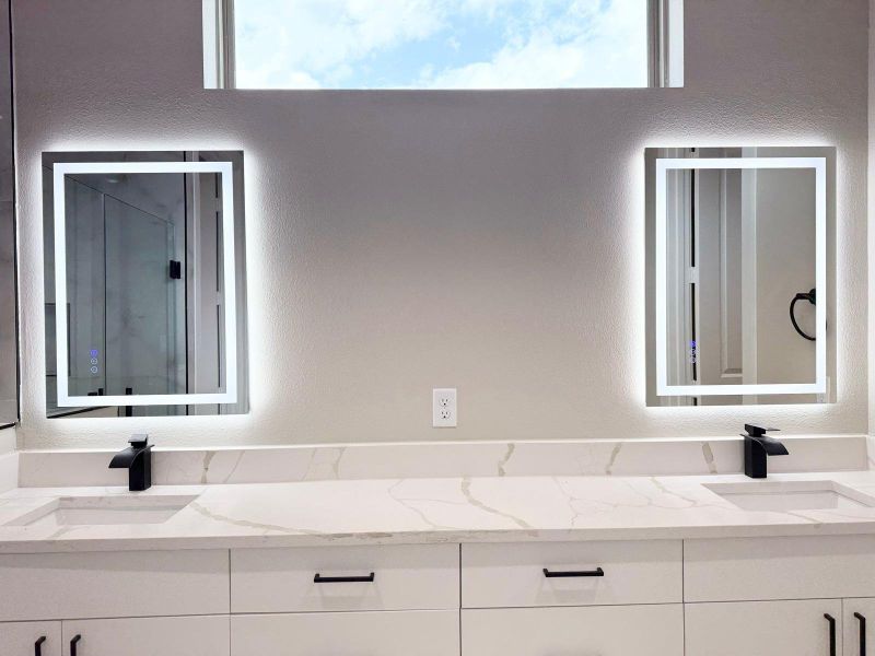 Luxurious primary bathroom with sleek, modern fixtures, dual backlit mirrors, and a spacious, elegant design.