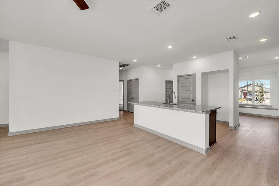 Kitchen with a kitchen island with sink, light stone counters, light wood finished floors, recessed lighting, and ceiling fan
