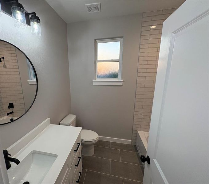 Full bathroom with toilet, tiled shower / bath, vanity, and tile patterned floors