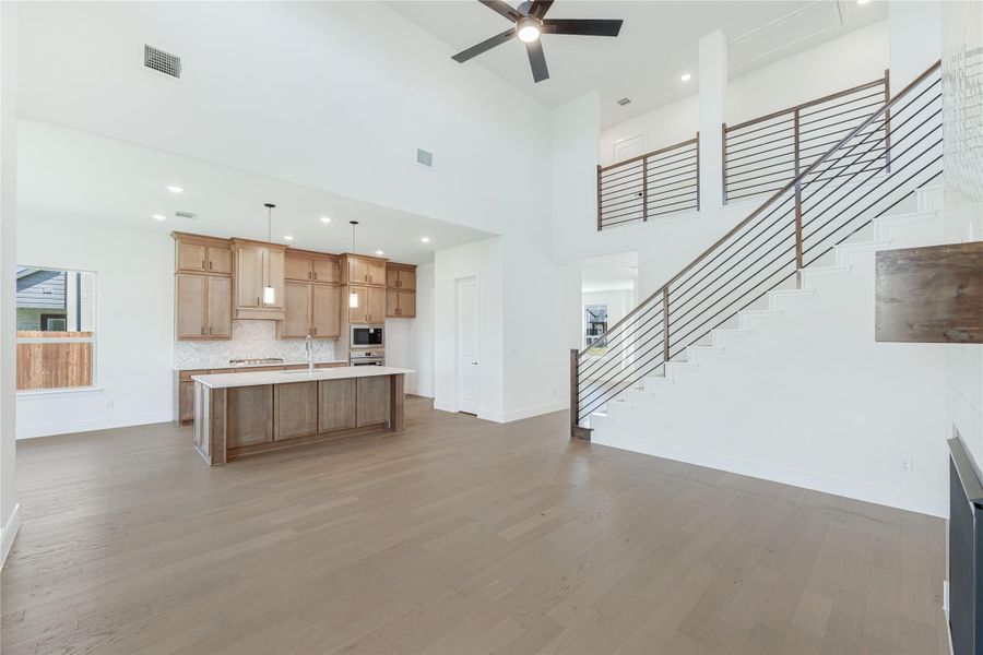 Open-concept living area with kitchen island, wood cabinets, hardwood floors, high ceiling, and staircase with metal railing.