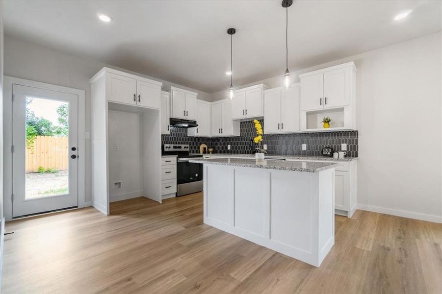 Kitchen with stainless steel electric range, backsplash, light stone counters, and light wood-type flooring