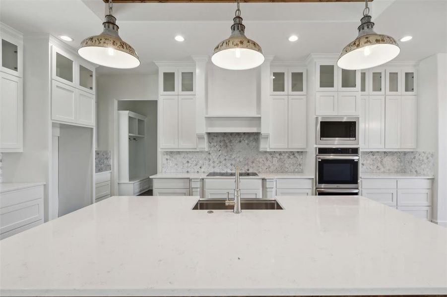 Kitchen featuring sink, decorative light fixtures, white cabinets, stainless steel microwave, and an island with sink