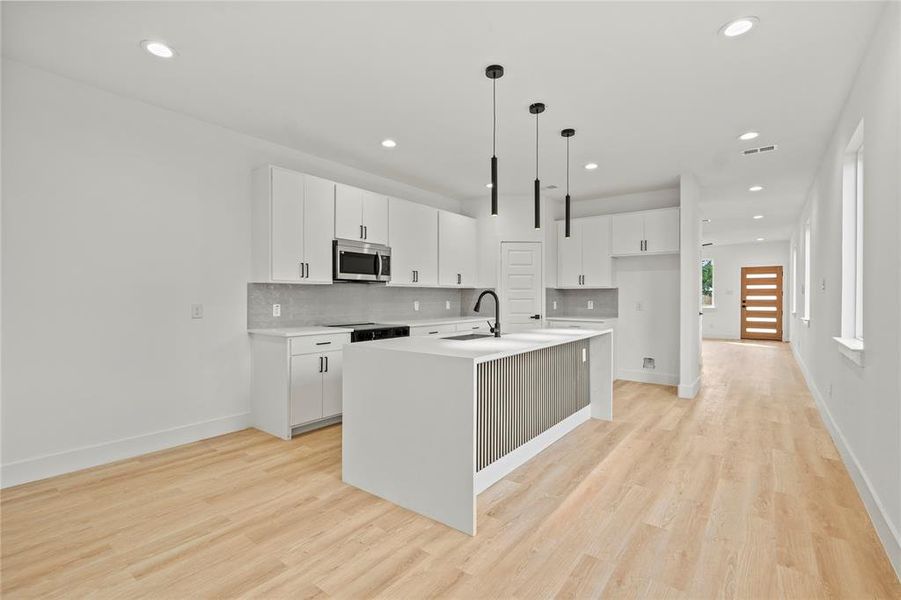 Kitchen featuring stainless steel microwave, tasteful backsplash, recessed lighting, light wood-style flooring, and an island with sink Kitchen featuring stainless steel microwave, tasteful backsplash, recessed lighting, light wood-style flooring, and an island with sink