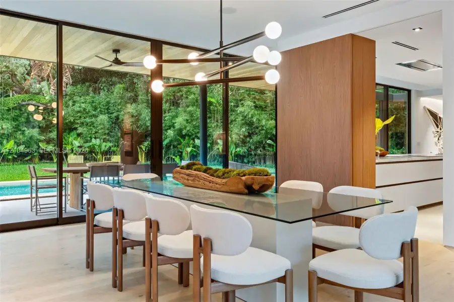 Floor-to-ceiling glass walls, wood-finish flooring, architectural multi-bulb chandelier, and wood-paneled feature wall