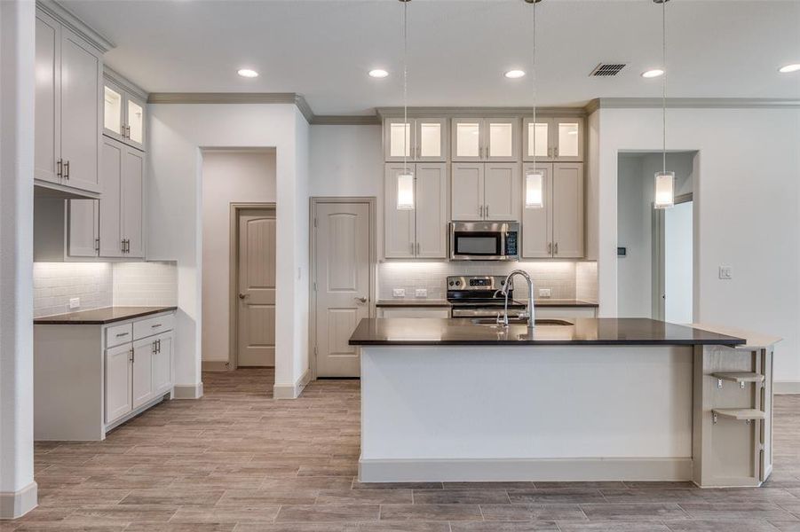 Kitchen with glass insert cabinets, decorative light fixtures, stainless steel appliances, tasteful backsplash, and crown molding Kitchen with glass insert cabinets, decorative light fixtures, stainless steel appliances, tasteful backsplash, and crown molding